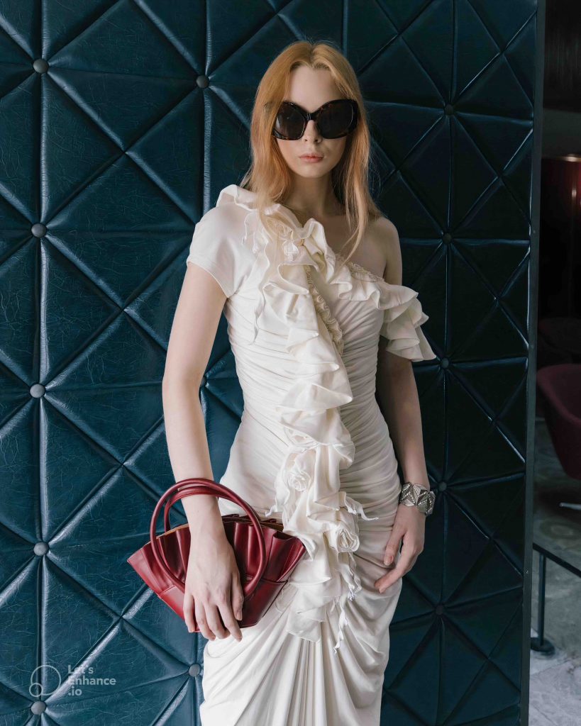 A woman in a white dress and sunglasses holds a red handbag