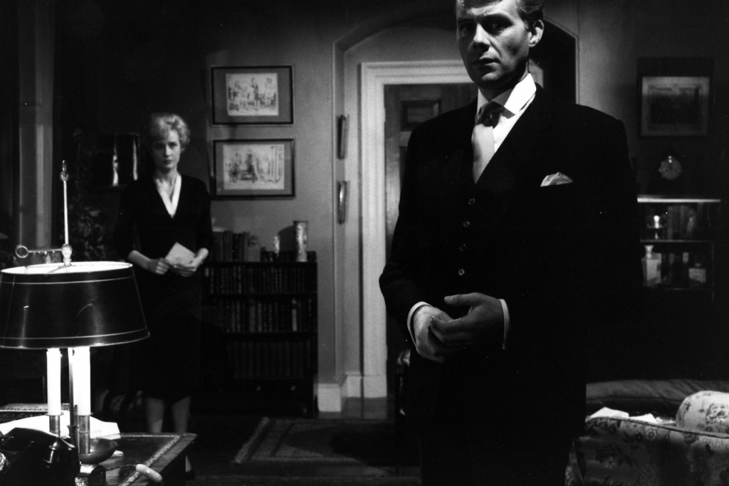 Một người đàn ông lịch lãm và một phụ nữ đứng trong căn phòng tối với đồ nội thất cổ điển