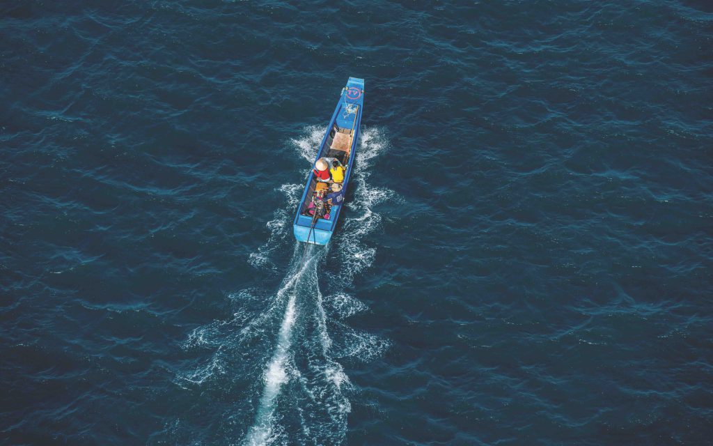A small blue fishing boat travels across a deep blue ocean