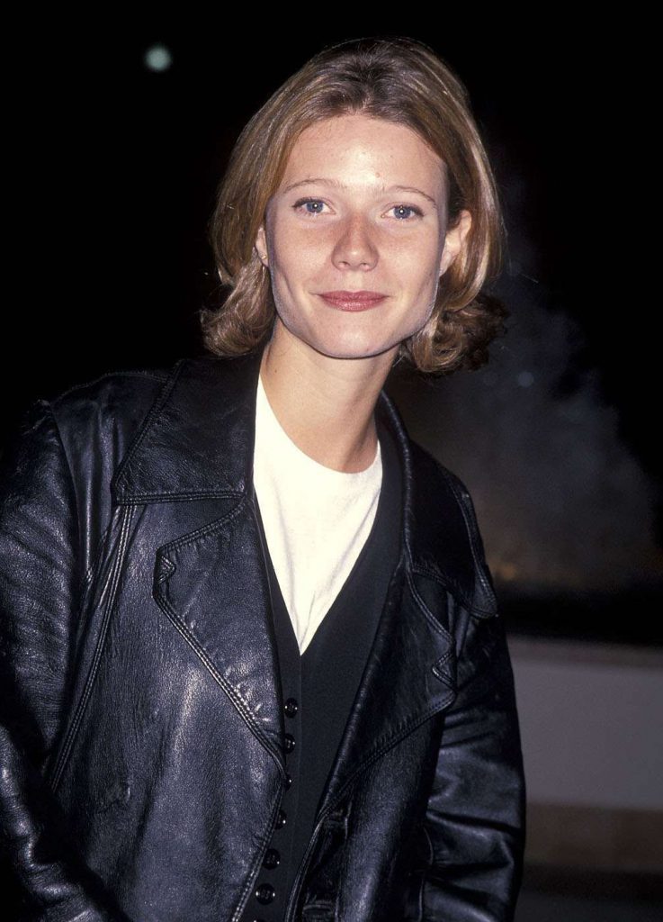 A woman with blonde hair wears a leather jacket and a white shirt