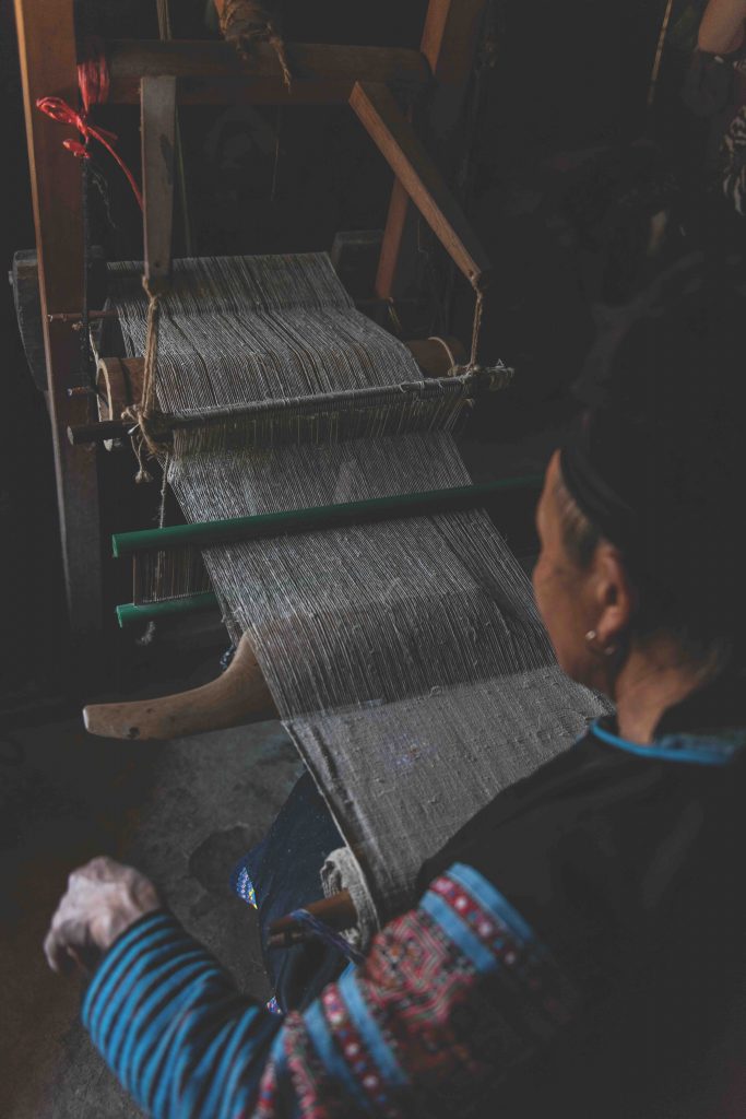 A weaver works at a wooden loom creating a striped textile