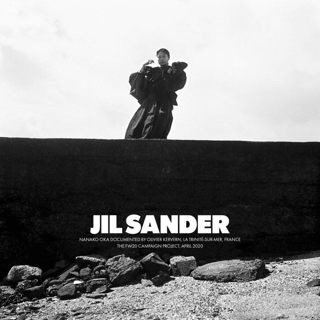 A model stands on a concrete structure near a rocky beach