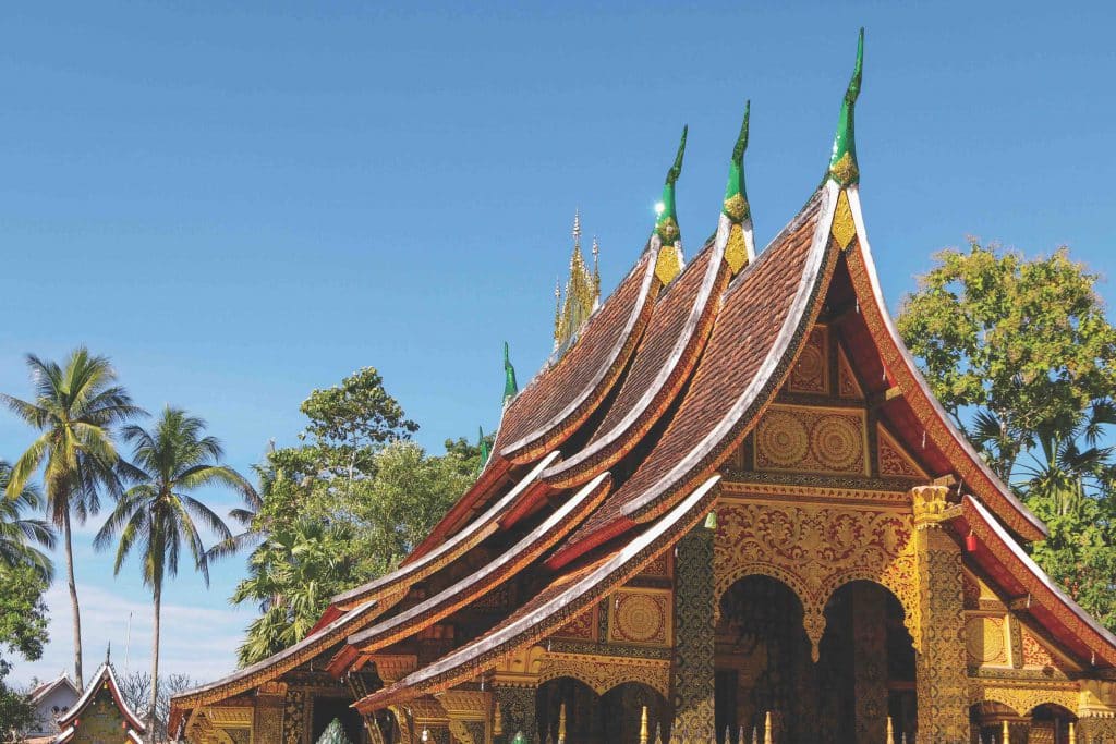 A golden temple roof with ornate details rises against a bright blue sky