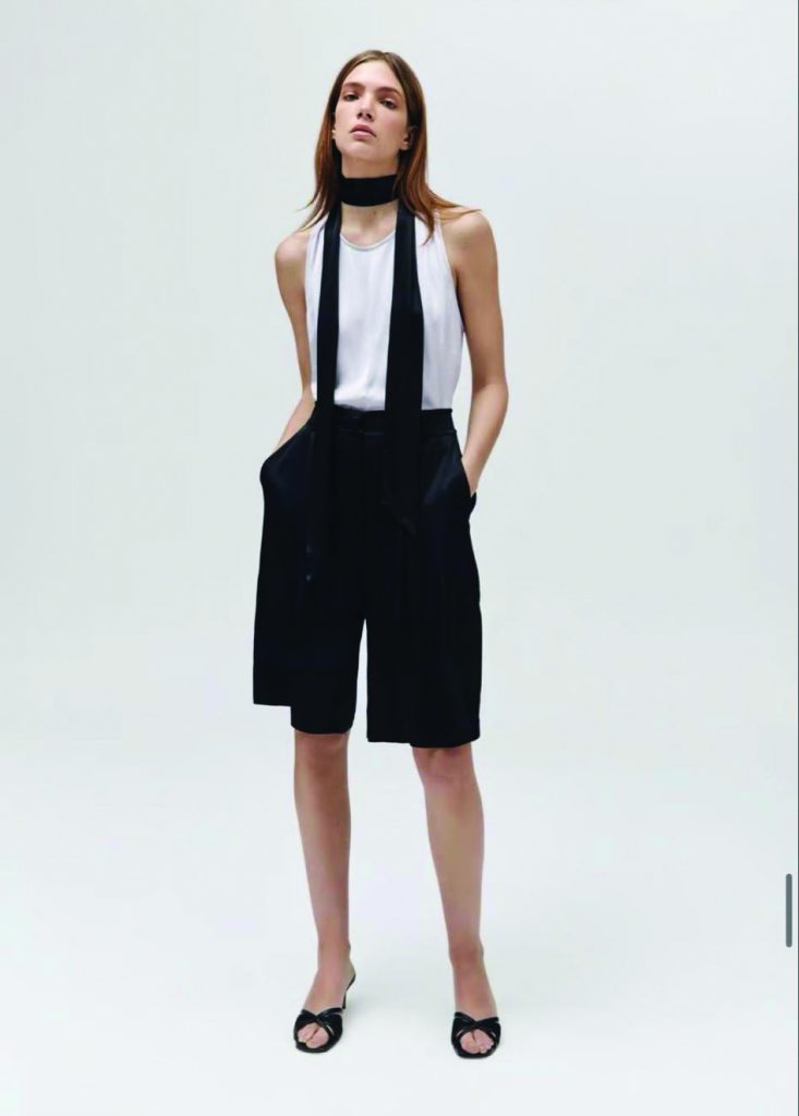 A woman models black shorts with suspenders a white halter top and a black choker necklace