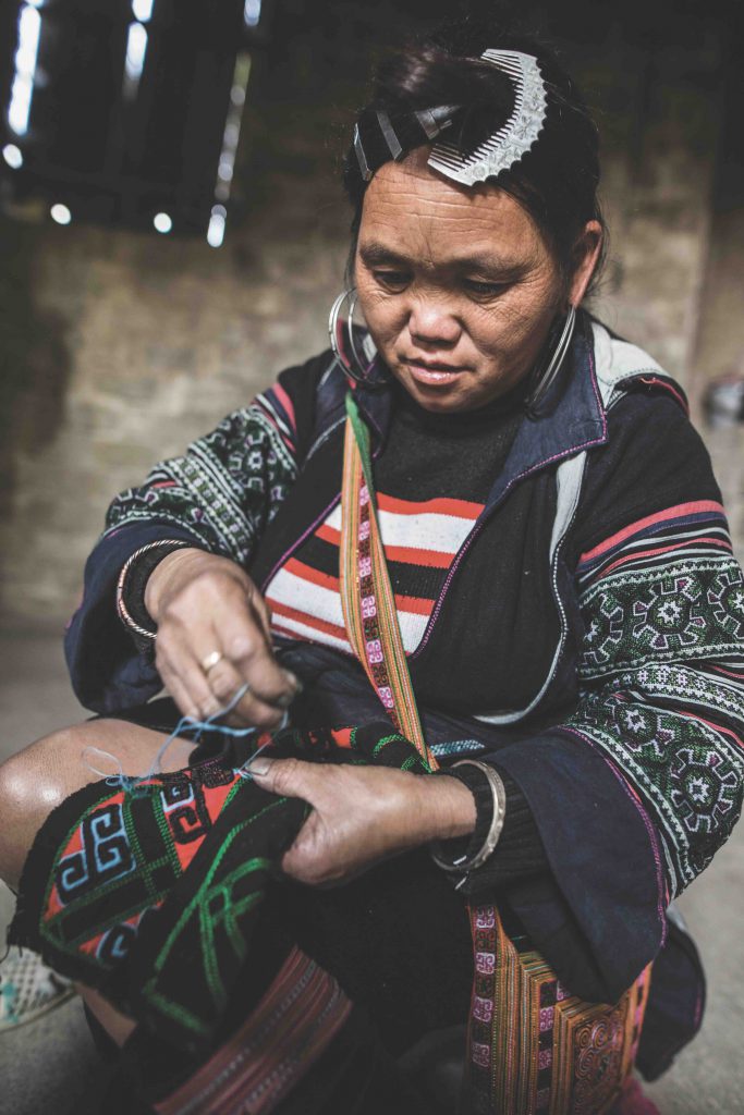 A woman in traditional clothing works on indigo dyed textiles