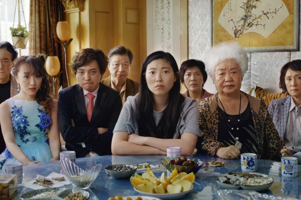 Một gia đình người châu Á ngồi xung quanh bàn đầy thức ăn với biểu cảm đa dạng