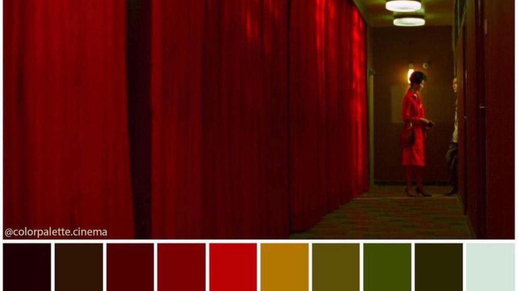 Người phụ nữ mặc áo đỏ đứng bên tấm rèm nhung đỏ trong căn phòng ánh vàng