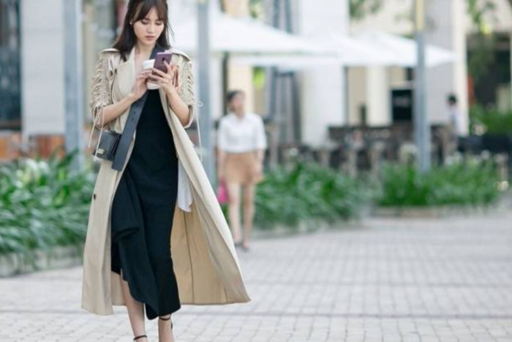 Cô gái trẻ dạo phố với áo khoác dài và đang sử dụng điện thoại