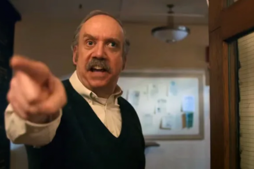 Giáo viên trung niên cau mày chỉ tay về phía người xem trong hành lang trường học